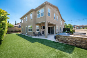 wo-story beige home with a balcony, large windows, green lawn, and stone retaining wall, Top Rental Demand Areas in Santa Clarita in 2026
