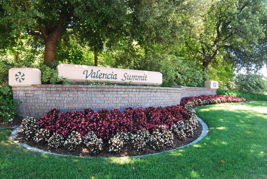 The Valencia Summit sign behind a large patch of lush, green grass and a flower bed that you see as you enter the Summit neighborhood